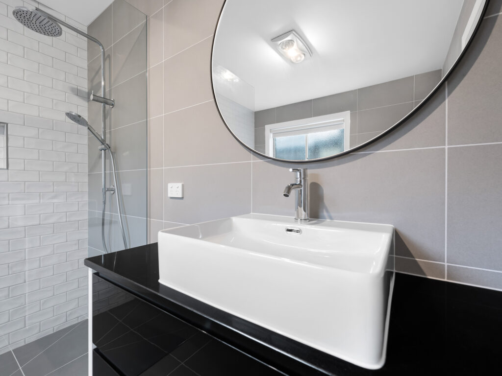 Modern vanity with round mirror and view of frameless shower