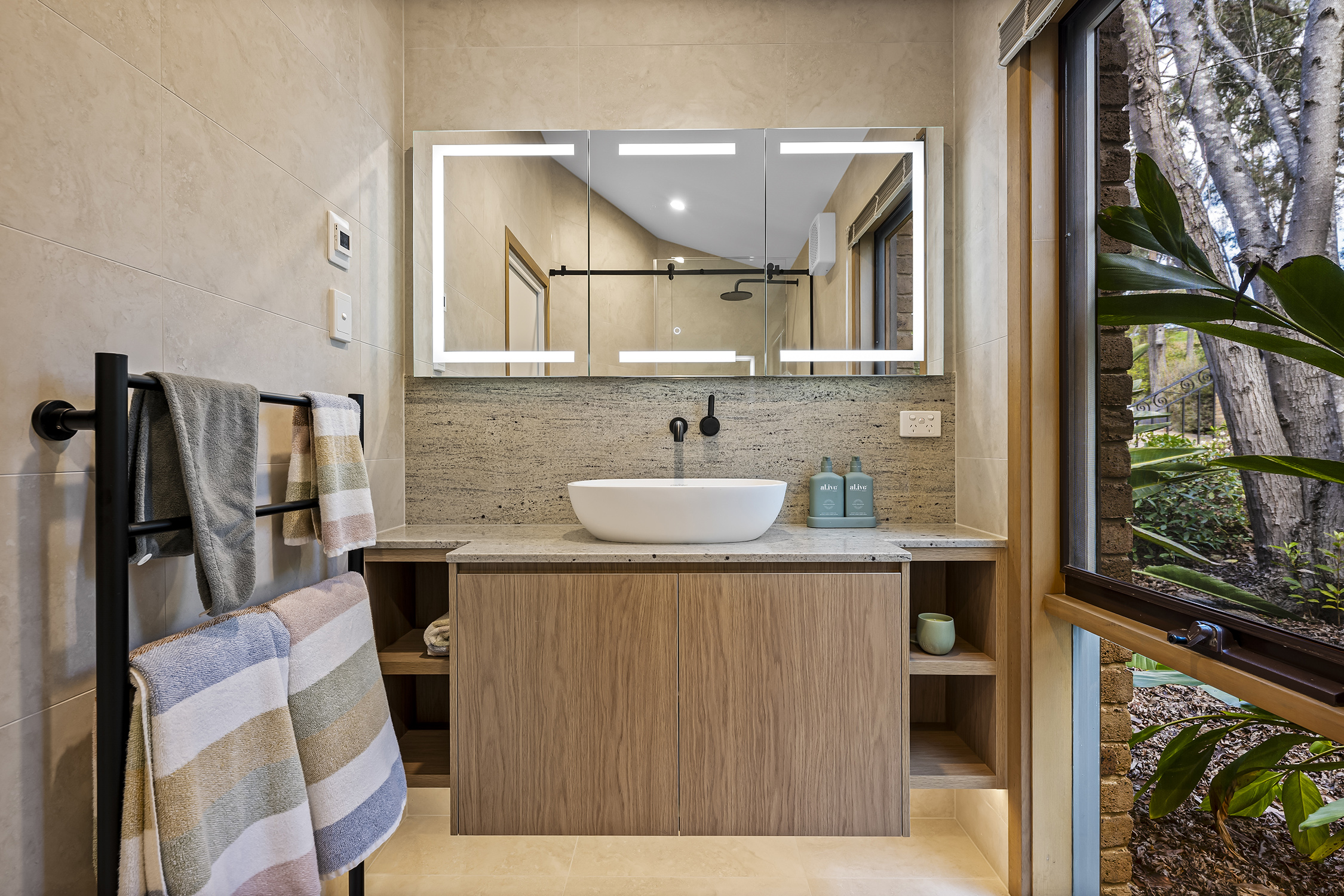 Close-up of vanity with vessel basin, stone splashback and matte black tapware.