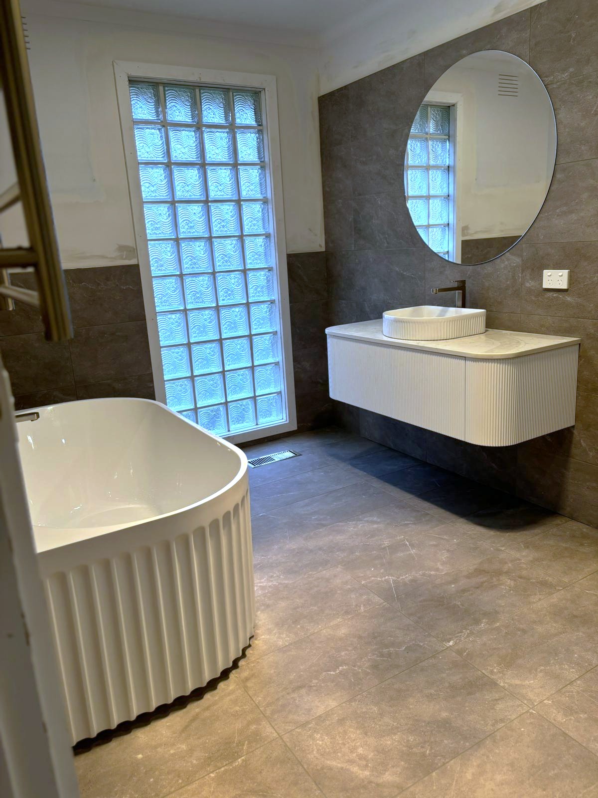 Fluted freestanding bath and custom wall-hung vanity with curved ribbed finish in modern bathroom