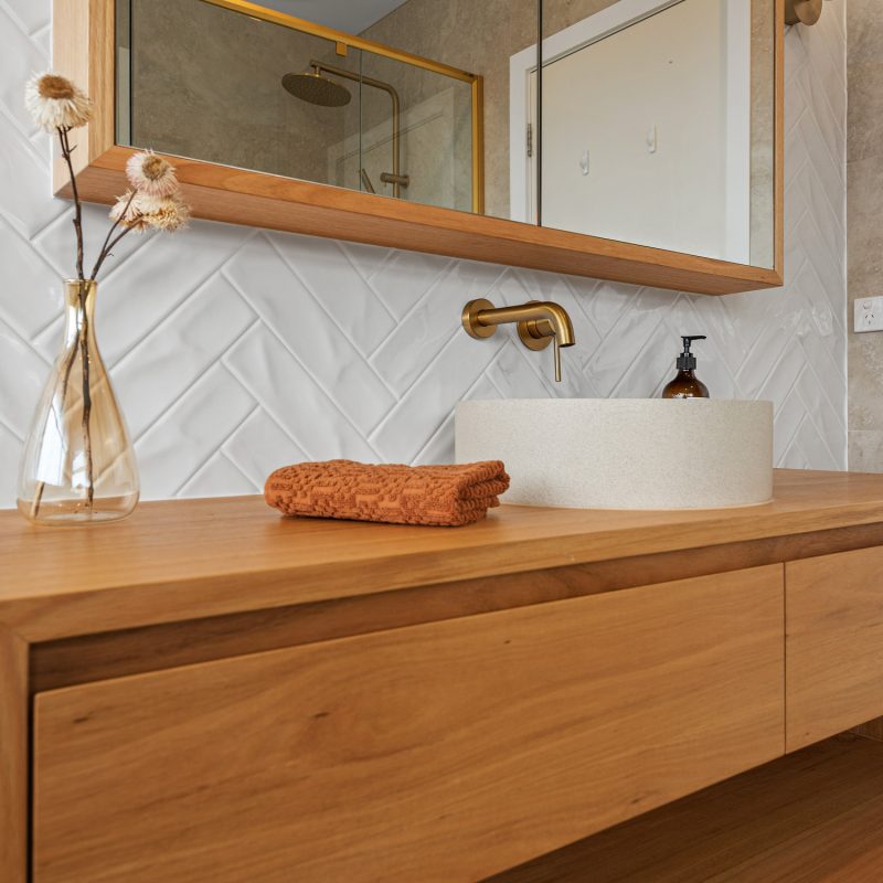Close-up of stone basin, herringbone tile splashback, and custom timber shaving cabinet.